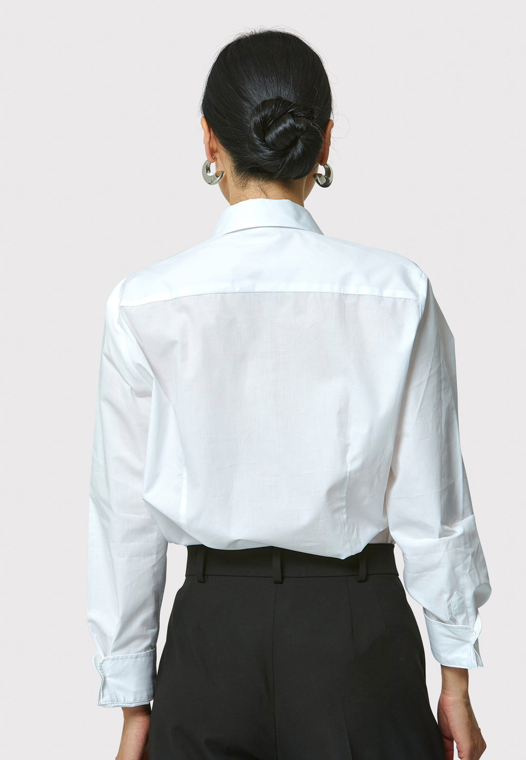 Person wearing a white shirt and black pants on a plain background