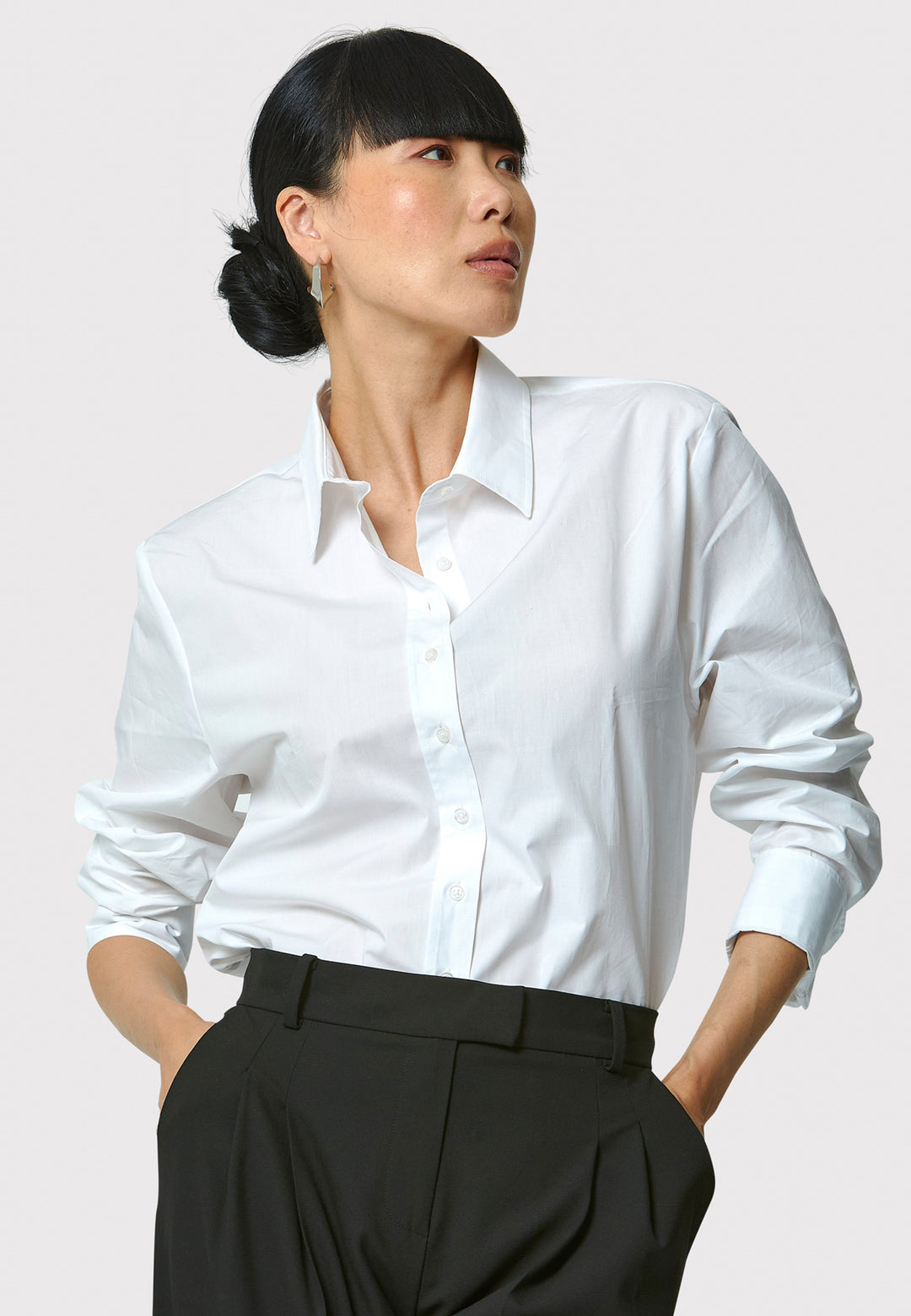 Woman wearing a white shirt and black pants against a plain background