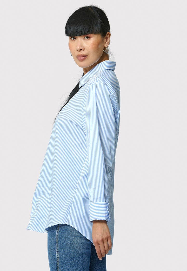 Woman wearing a light blue striped shirt and jeans on a plain background