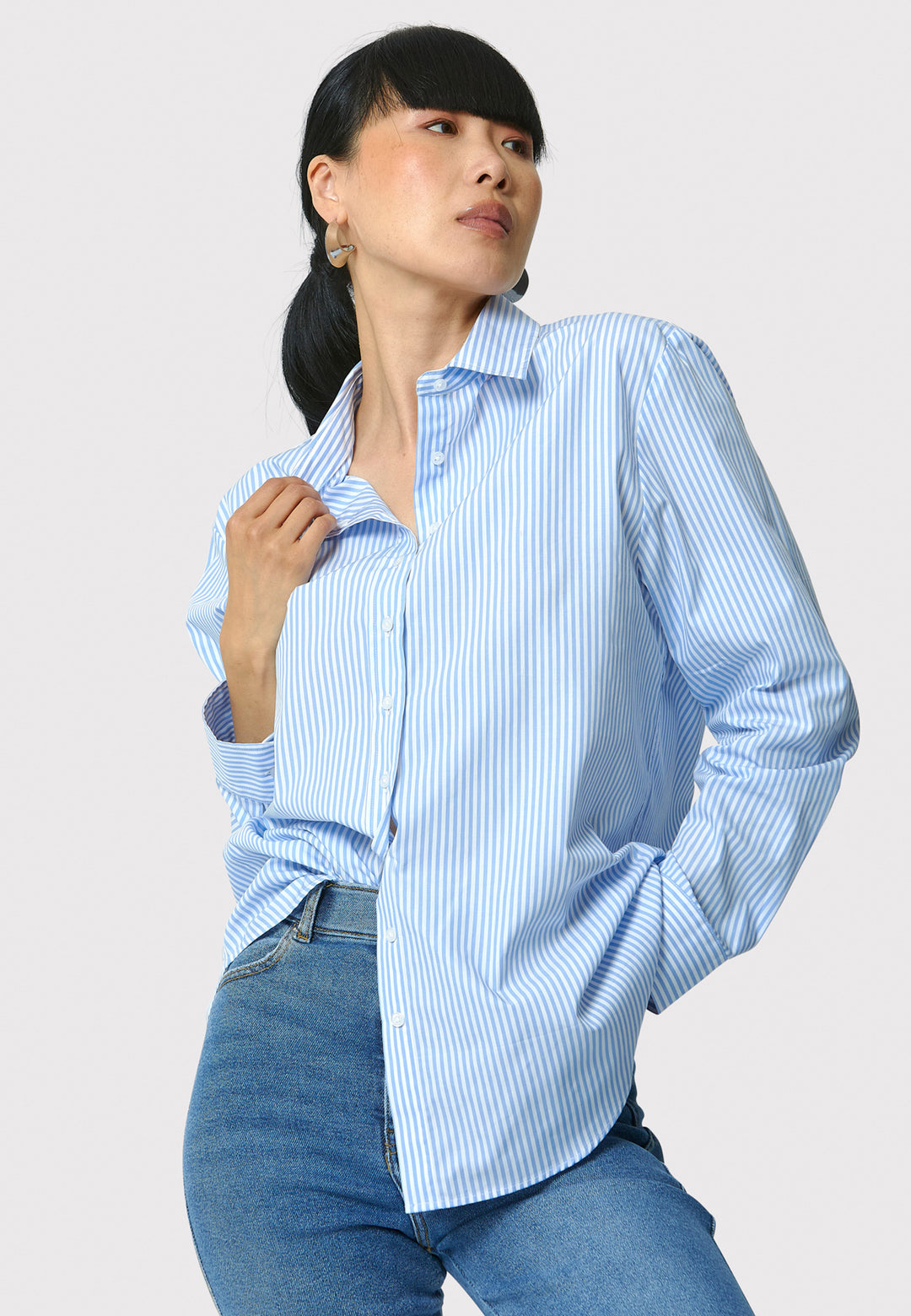 Woman wearing a light blue striped shirt and jeans on a white background