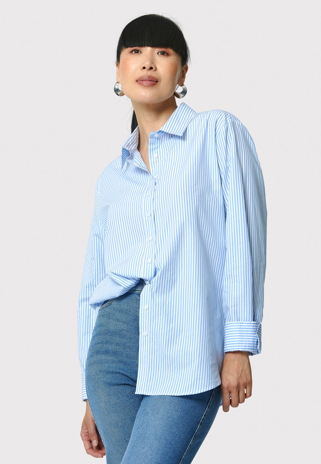 Woman wearing a light blue striped shirt and jeans on a white background