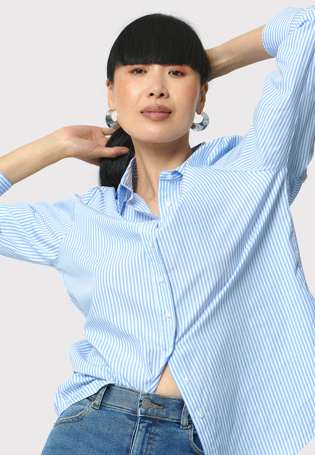 Woman wearing a light blue striped shirt and jeans against a plain background