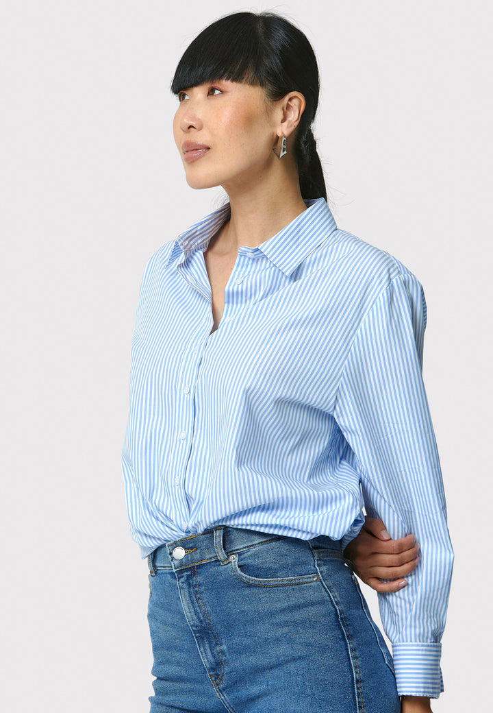 Woman wearing a light blue striped shirt and jeans against a white background