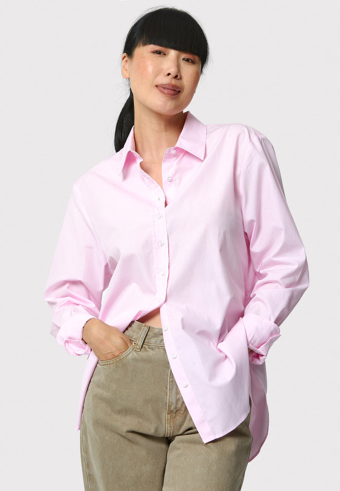 Woman wearing a light pink shirt and beige pants on a plain background