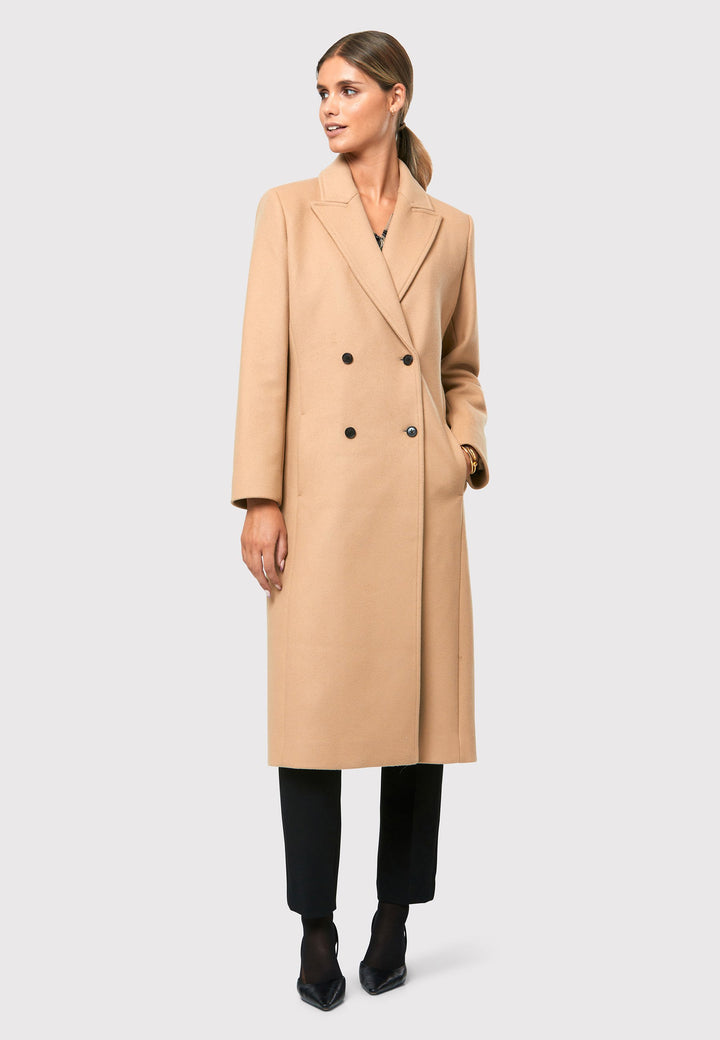 classic double-breasted coat silhouette adorned with four elegant brown horn buttons, perfectly complementing the sand color. The coat features a sleek collar and revere design. Crafted from luxurious melton fabric, it falls gracefully below the knee, enveloping you in both comfort and sophistication. 