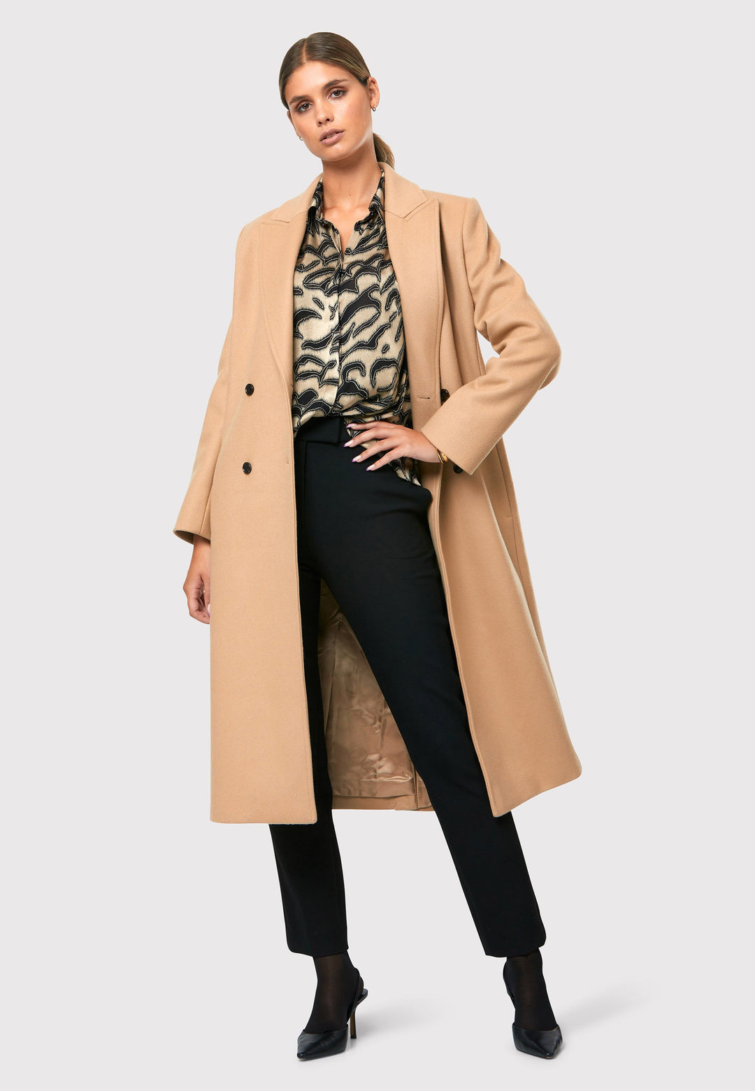 classic double-breasted coat silhouette adorned with four elegant brown horn buttons, perfectly complementing the sand color. The coat features a sleek collar and revere design. Crafted from luxurious melton fabric, it falls gracefully below the knee, enveloping you in both comfort and sophistication. 
