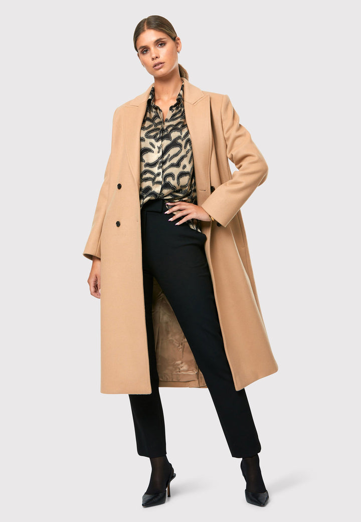 classic double-breasted coat silhouette adorned with four elegant brown horn buttons, perfectly complementing the sand color. The coat features a sleek collar and revere design. Crafted from luxurious melton fabric, it falls gracefully below the knee, enveloping you in both comfort and sophistication. 
