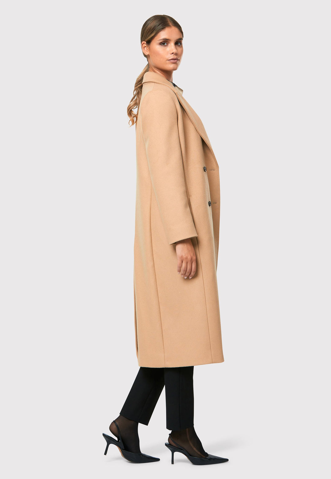 classic double-breasted coat silhouette adorned with four elegant brown horn buttons, perfectly complementing the sand color. The coat features a sleek collar and revere design. Crafted from luxurious melton fabric, it falls gracefully below the knee, enveloping you in both comfort and sophistication. 