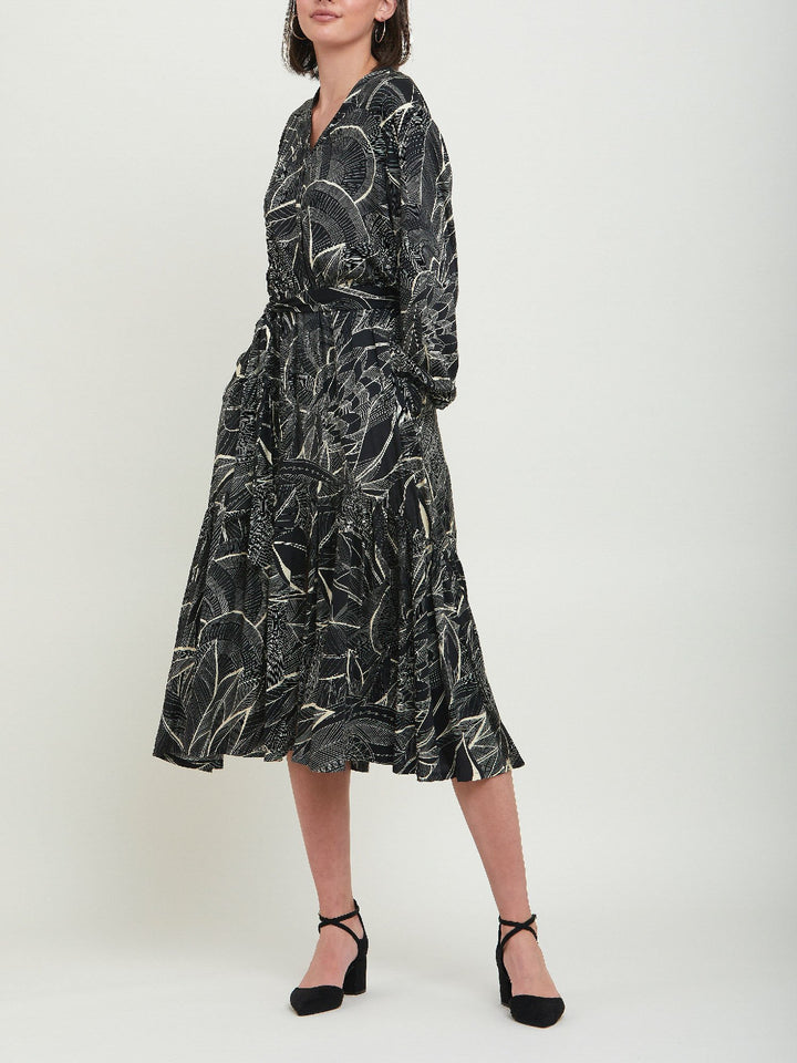 Beverly, an everyday dress. Crafted in a fluid, cream on black, botanical print viscose. A simple style with a V-neck button down bodice, handy pockets, elasticated waist & matching belt. Dress offers voluminous sleeves & a centre front slit on a fluid tiered skirt which falls to the mid-calf. 