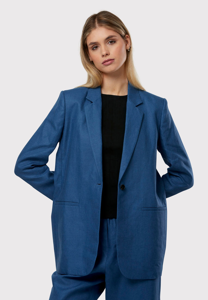 Cassie, the investment-worthy borage blue linen blazer. The epitome of summer sophistication. Minimalist styling accentuated by a single button fastening and an oversized, slightly boxy silhouette. Pair it effortlessly with a simple tee and the coordinating Vanessa pant, finished with trainers for a chic and contemporary ensemble.