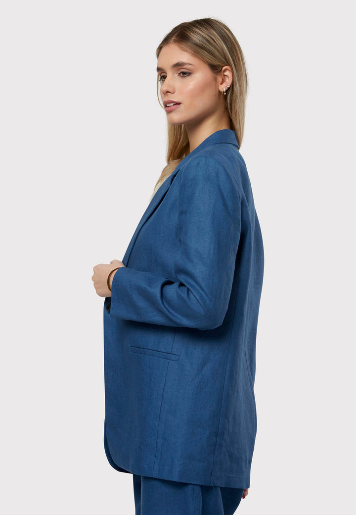 Cassie, the investment-worthy borage blue linen blazer. The epitome of summer sophistication. Minimalist styling accentuated by a single button fastening and an oversized, slightly boxy silhouette. Pair it effortlessly with a simple tee and the coordinating Vanessa pant, finished with trainers for a chic and contemporary ensemble.