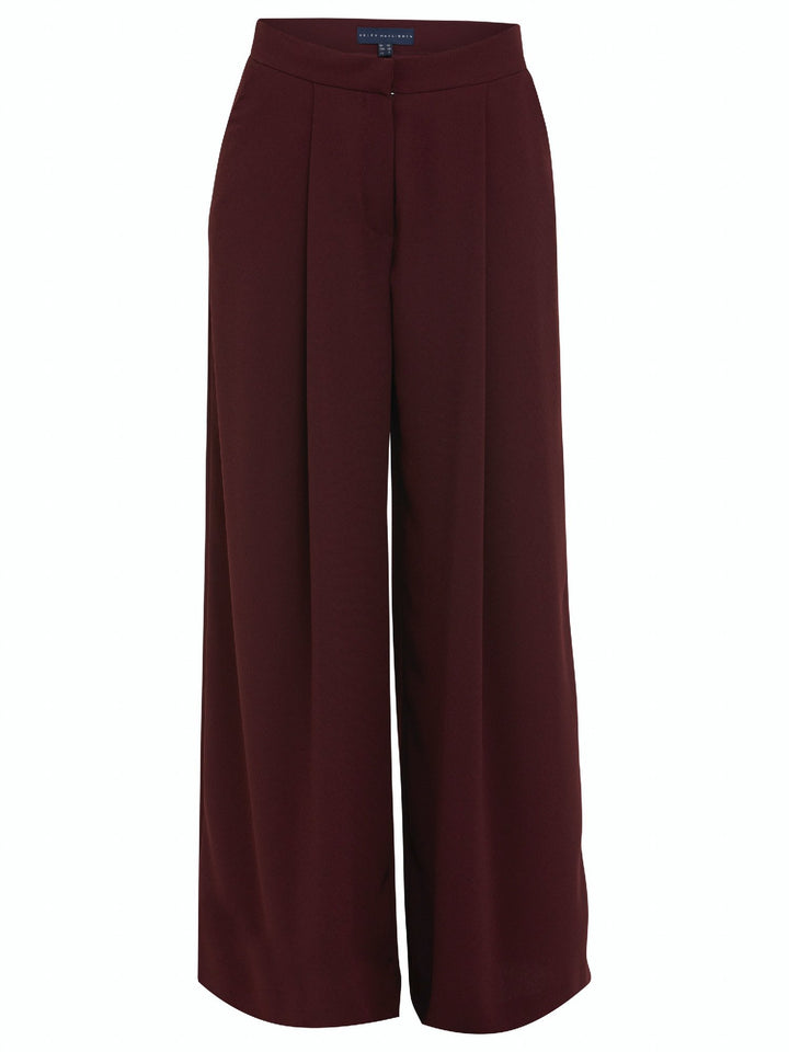 Charlize, a wide-leg palazzo pant. Crafted in a satin back crepe in rich burgundy. Features deep pleats, sharp front crease & side pockets. A high-waisted trouser made to take you from desk to dinner with a relaxed & refined silhouette. Style with flats or dress up with heels.