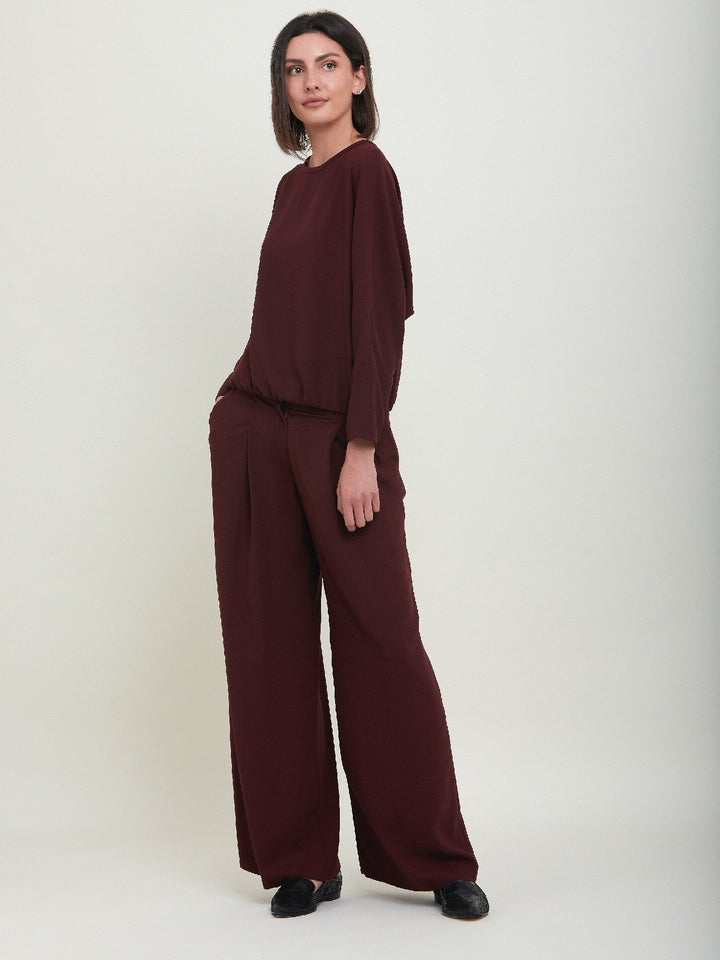 Charlize, a wide-leg palazzo pant. Crafted in a satin back crepe in rich burgundy. Features deep pleats, sharp front crease & side pockets. A high-waisted trouser made to take you from desk to dinner with a relaxed & refined silhouette. Style with flats or dress up with heels.