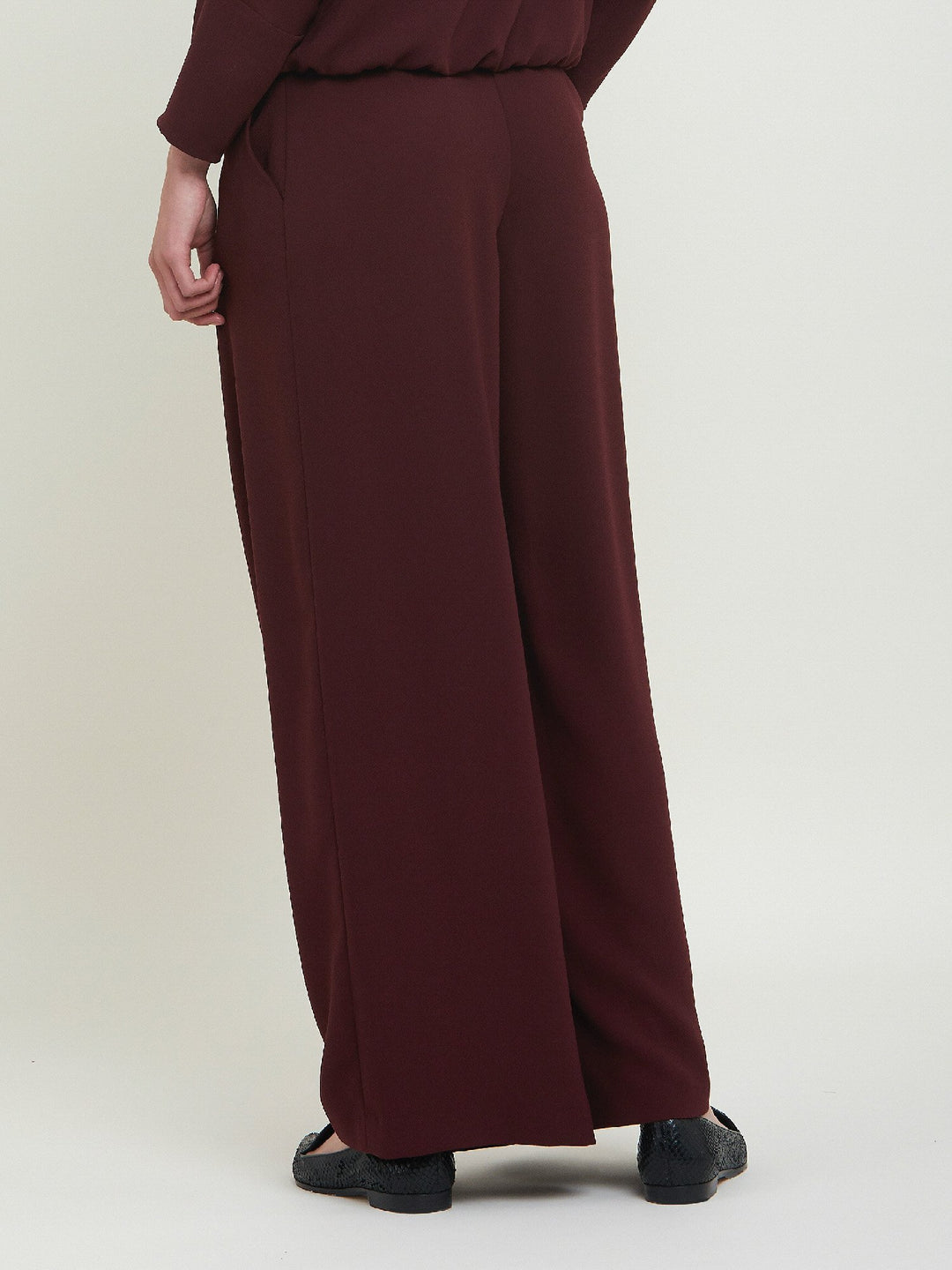 Charlize, a wide-leg palazzo pant. Crafted in a satin back crepe in rich burgundy. Features deep pleats, sharp front crease & side pockets. A high-waisted trouser made to take you from desk to dinner with a relaxed & refined silhouette. Style with flats or dress up with heels.
