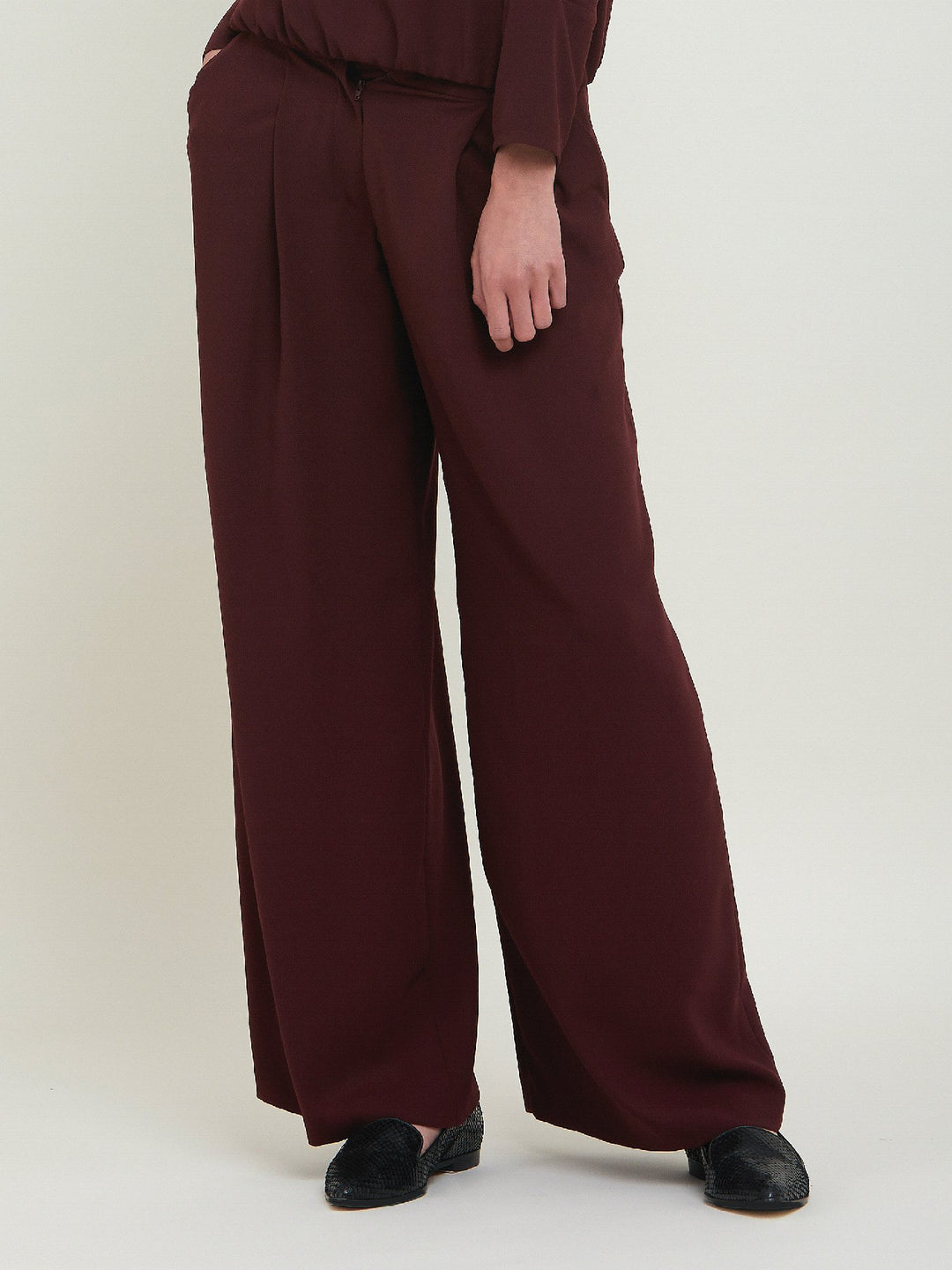 Charlize, a wide-leg palazzo pant. Crafted in a satin back crepe in rich burgundy. Features deep pleats, sharp front crease & side pockets. A high-waisted trouser made to take you from desk to dinner with a relaxed & refined silhouette. Style with flats or dress up with heels.