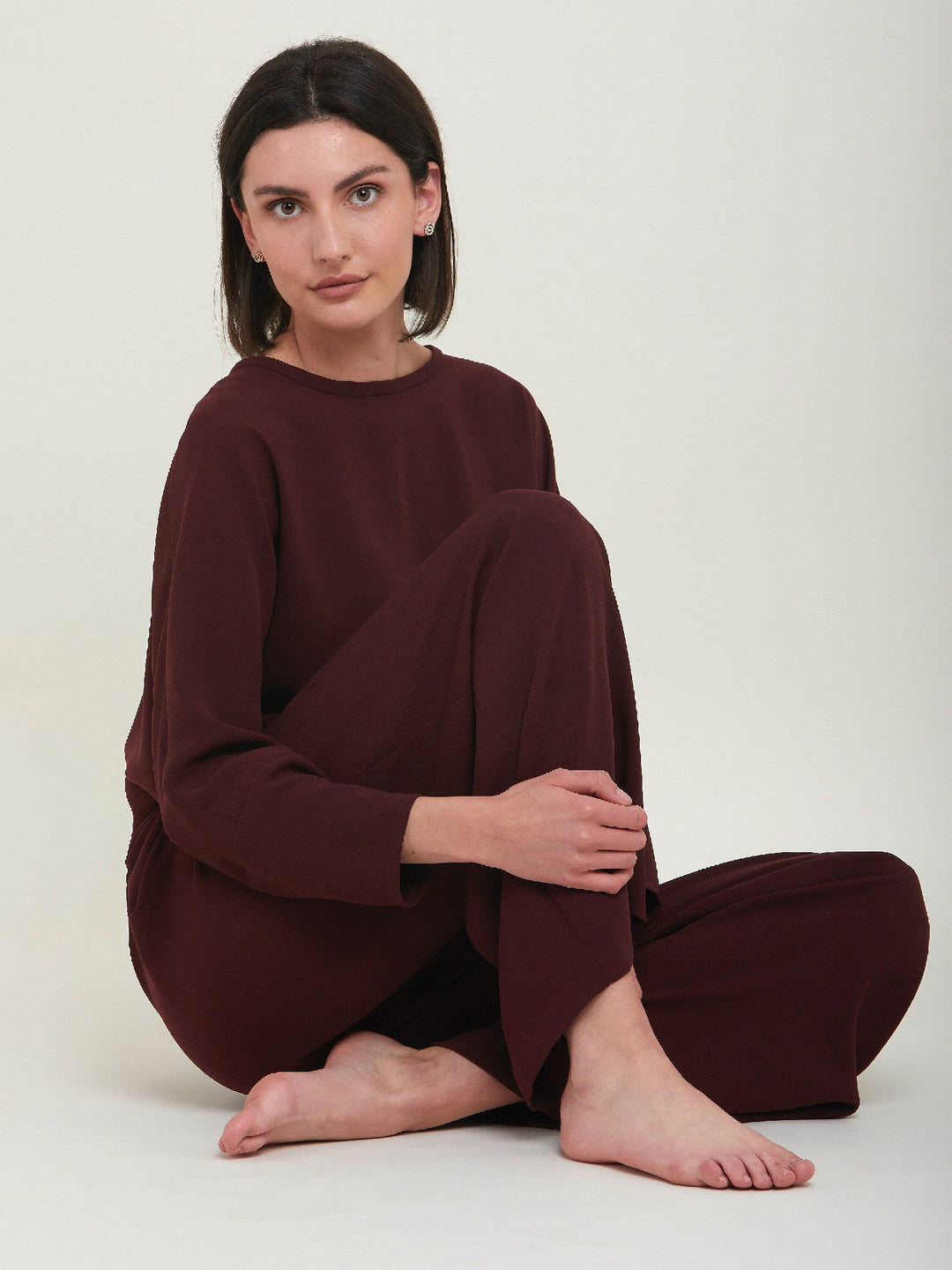 Charlize, a wide-leg palazzo pant. Crafted in a satin back crepe in rich burgundy. Features deep pleats, sharp front crease & side pockets. A high-waisted trouser made to take you from desk to dinner with a relaxed & refined silhouette. Style with flats or dress up with heels.