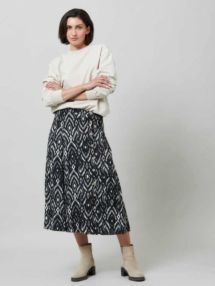 Meet saddie, the essential transeasonal skirt. Crafted in a fluid black and cream ikat printed viscose.. Off centered button through a-line silhouette with an elasticated back waist band. Relaxed elegance for everyday life. Style with our black timeless tops or dress it down with the khloe oatmeal sweatshirt.
