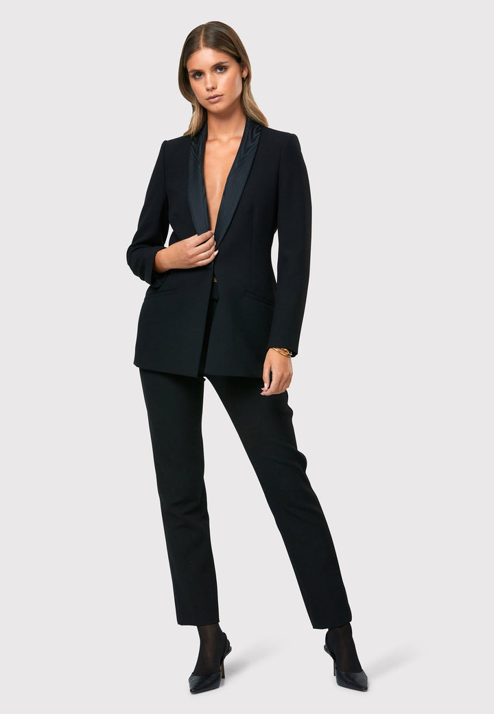Discover the Darcie Black Jacket, an essential piece for any minimalist wardrobe. This exquisitely crafted tuxedo jacket is a timeless investment, featuring a traditional shawl collar and sleek welt pockets. Its semi-fitted silhouette, accentuated by a single button closure, offers a flattering look. Meticulously tailored from our renowned fabric, this jacket ensures both comfort and flexibility with a touch of stretch.