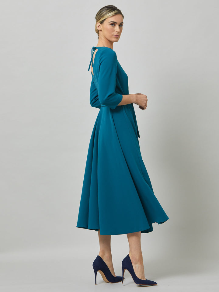 Eva, inspired by hollywood glamour. Crafted in an atlantic teal tricotine with a touch of stretch. features a flattering scoop back detail, semi-circular skirt with pockets that falls the mid-calf. Waisted with a detachable belt. A winter wedding essential!