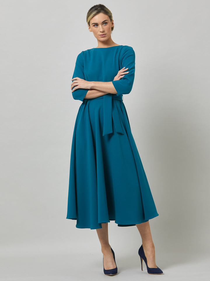 Eva, inspired by hollywood glamour. Crafted in an atlantic teal tricotine with a touch of stretch. features a flattering scoop back detail, semi-circular skirt with pockets that falls the mid-calf. Waisted with a detachable belt. A winter wedding essential!