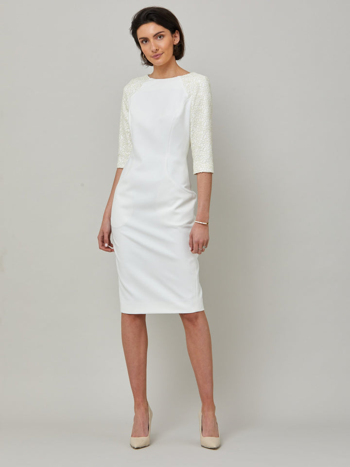 front picture of model wearing Juliet, A form-flattering, body-skimming silhouette in iconic white. Features a 3/4 sleeve with lace overlay. The skirt falls to a demure finish below the knee. Attending a summer wedding? Mother of the bride? Heading to the races? This is the dress for you.