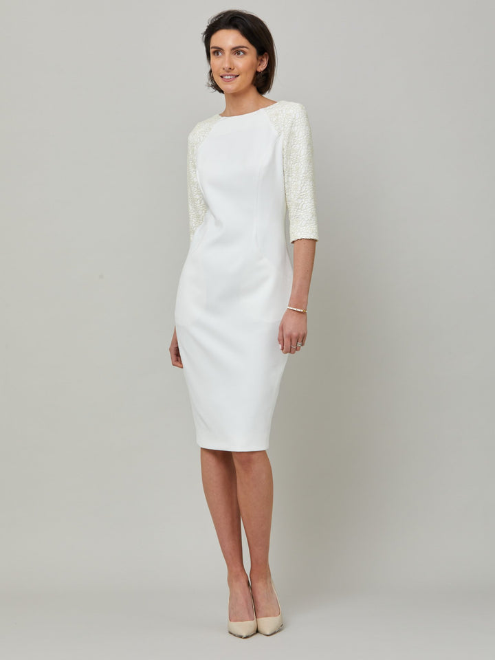 model wearing Juliet, A form-flattering, body-skimming silhouette in iconic white. Features a 3/4 sleeve with lace overlay. The skirt falls to a demure finish below the knee. Attending a summer wedding? Mother of the bride? Heading to the races? This is the dress for you.