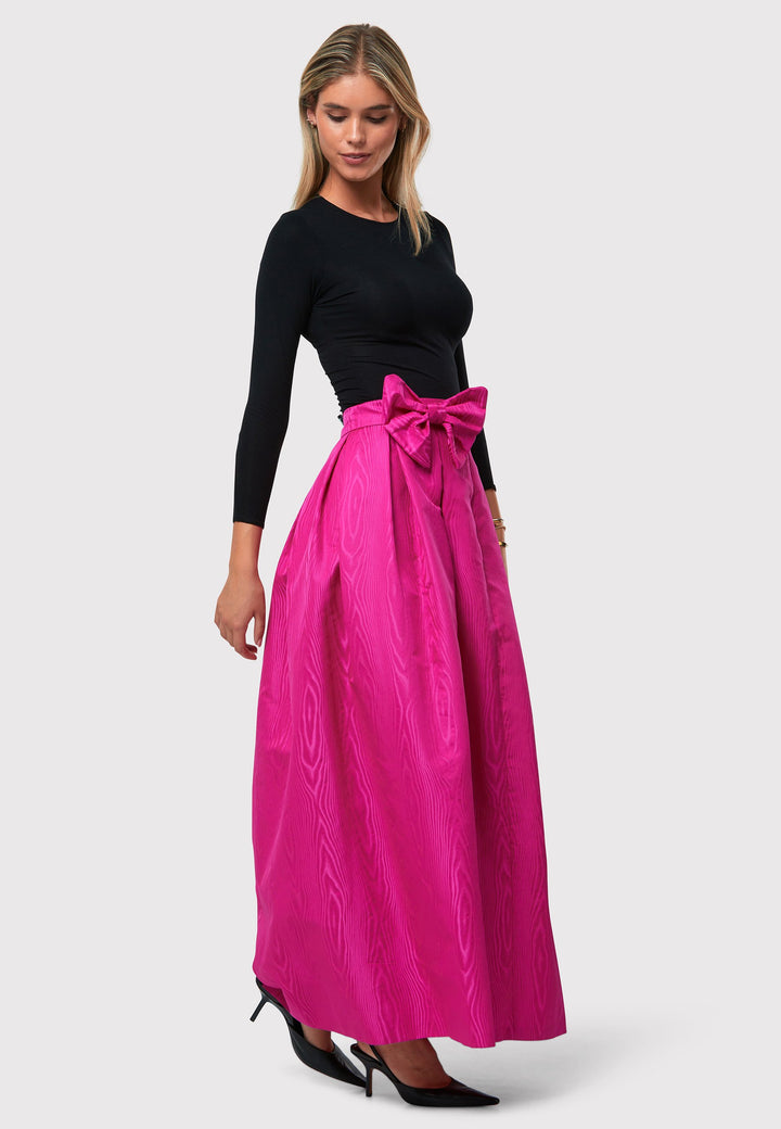 Introducing the Kennedy Cerise Pink Skirt, a sophisticated and chic piece inspired by 1950s fashion. This full-length A-line skirt features a stiff structure, reminiscent of the iconic 50s style. The moire pattern adds a unique and elegant touch to the design, creating a captivating visual effect. Complete with pleats around the waistline and a detachable bow belt, this skirt captures the essence of timeless glamour. 