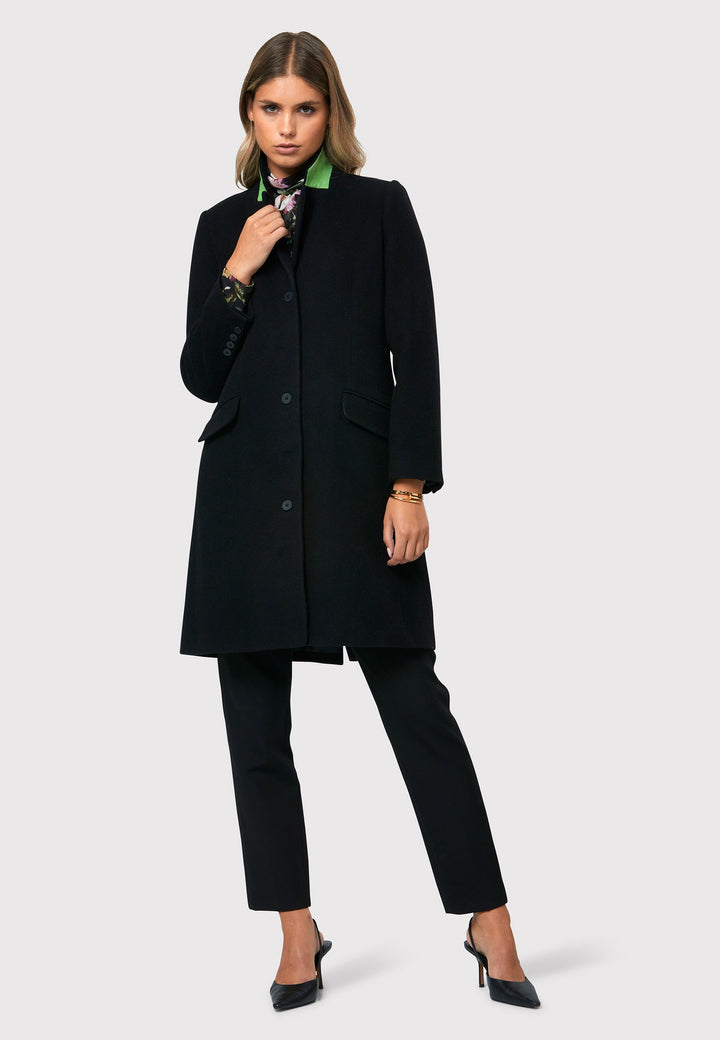 Introducing the Leighton Black Coat, a stylish and sophisticated wardrobe investment. Crafted from a wool and cashmere blend melton, this knee-length coat offers both warmth and style. Inspired by refined men's tailoring, it features a tidy collar and revere. The coat also boasts a striking bright green undercollar, adding a touch of uniqueness and visual interest.