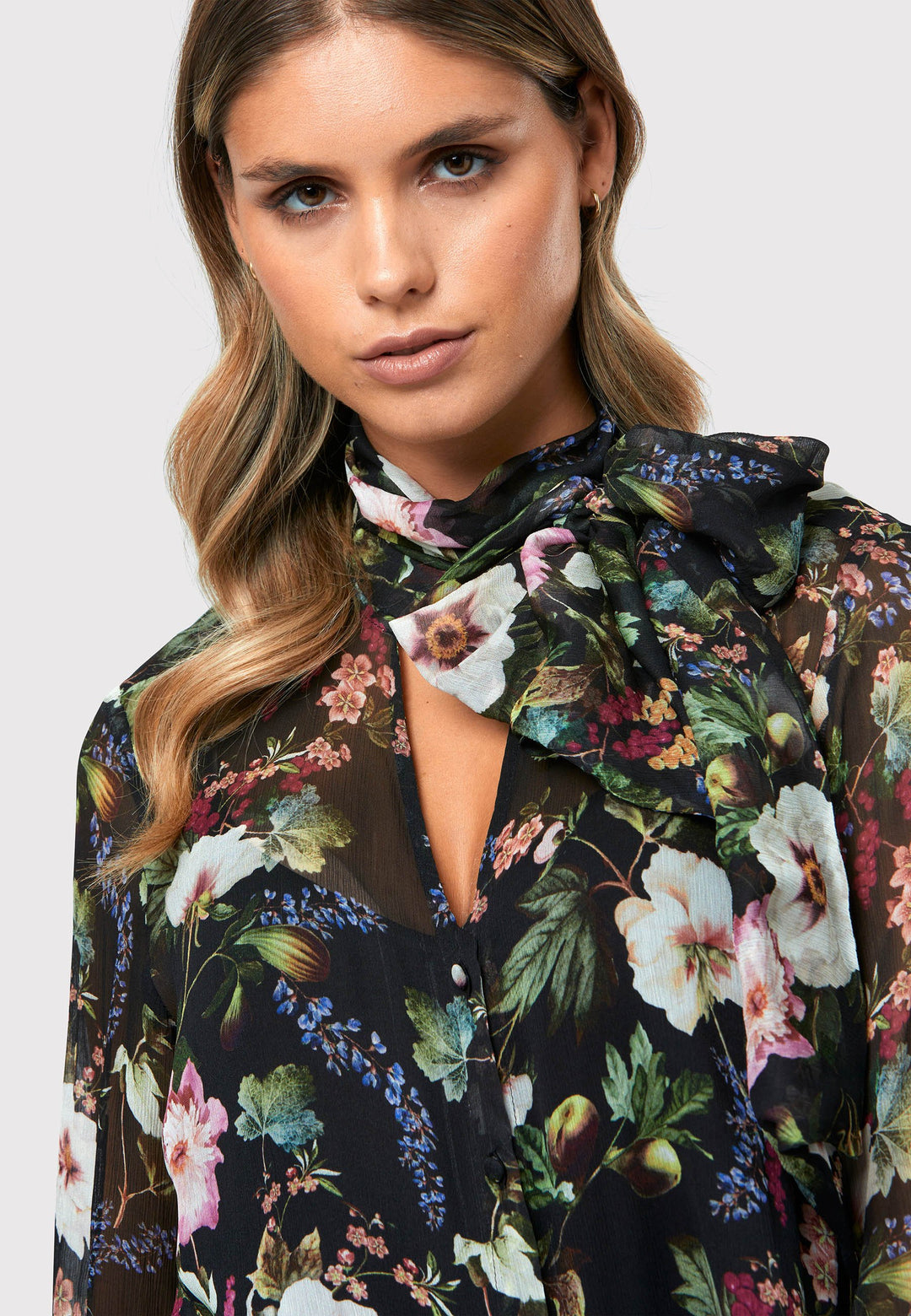 Introducing the Lorelei Floral Noir Print Blouse, a captivating blend of elegance and versatility. This blouse showcases a beautiful black-based floral print, adding a touch of sophistication to any outfit. The pussy bow neck tie, atop a flattering v-neckline, offers a versatile styling option. Wear it tied for a polished and feminine look or leave it down for a more relaxed feel. The button-down front adds a classic element, while the full-length sleeves and thick button-down cuffs exude refinement. 