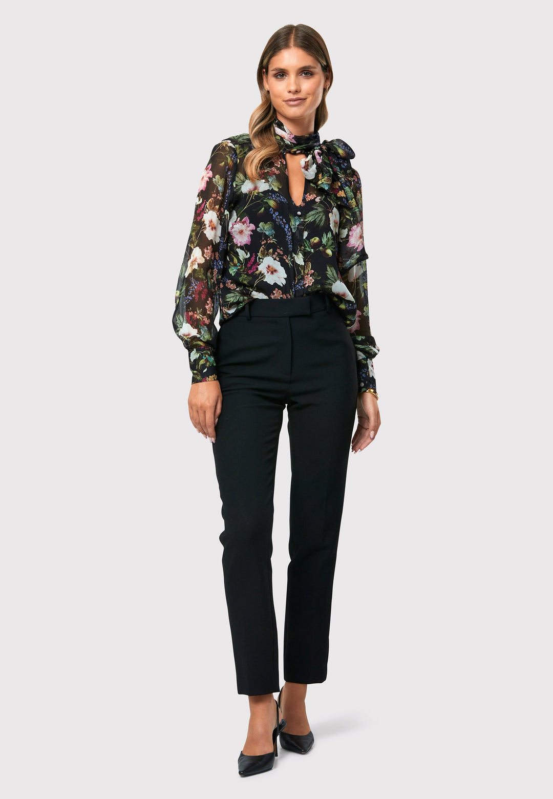 Introducing the Lorelei Floral Noir Print Blouse, a captivating blend of elegance and versatility. This blouse showcases a beautiful black-based floral print, adding a touch of sophistication to any outfit. The pussy bow neck tie, atop a flattering v-neckline, offers a versatile styling option. Wear it tied for a polished and feminine look or leave it down for a more relaxed feel. The button-down front adds a classic element, while the full-length sleeves and thick button-down cuffs exude refinement. 