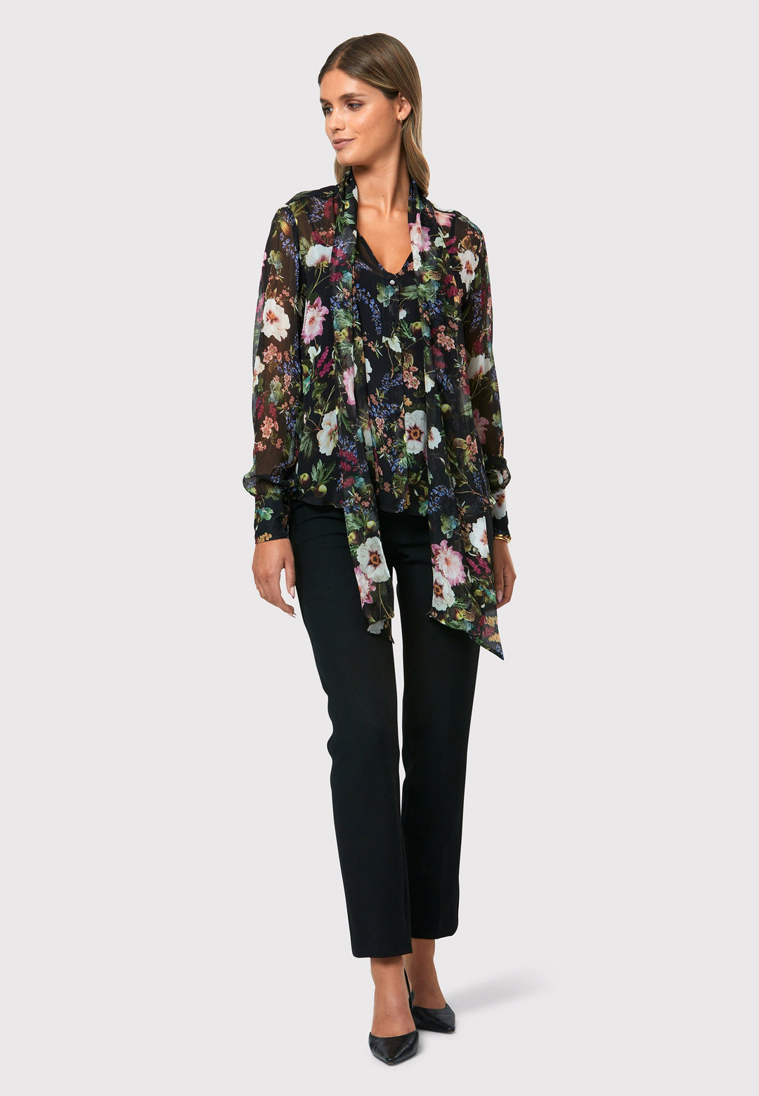 Introducing the Lorelei Floral Noir Print Blouse, a captivating blend of elegance and versatility. This blouse showcases a beautiful black-based floral print, adding a touch of sophistication to any outfit. The pussy bow neck tie, atop a flattering v-neckline, offers a versatile styling option. Wear it tied for a polished and feminine look or leave it down for a more relaxed feel. The button-down front adds a classic element, while the full-length sleeves and thick button-down cuffs exude refinement. 