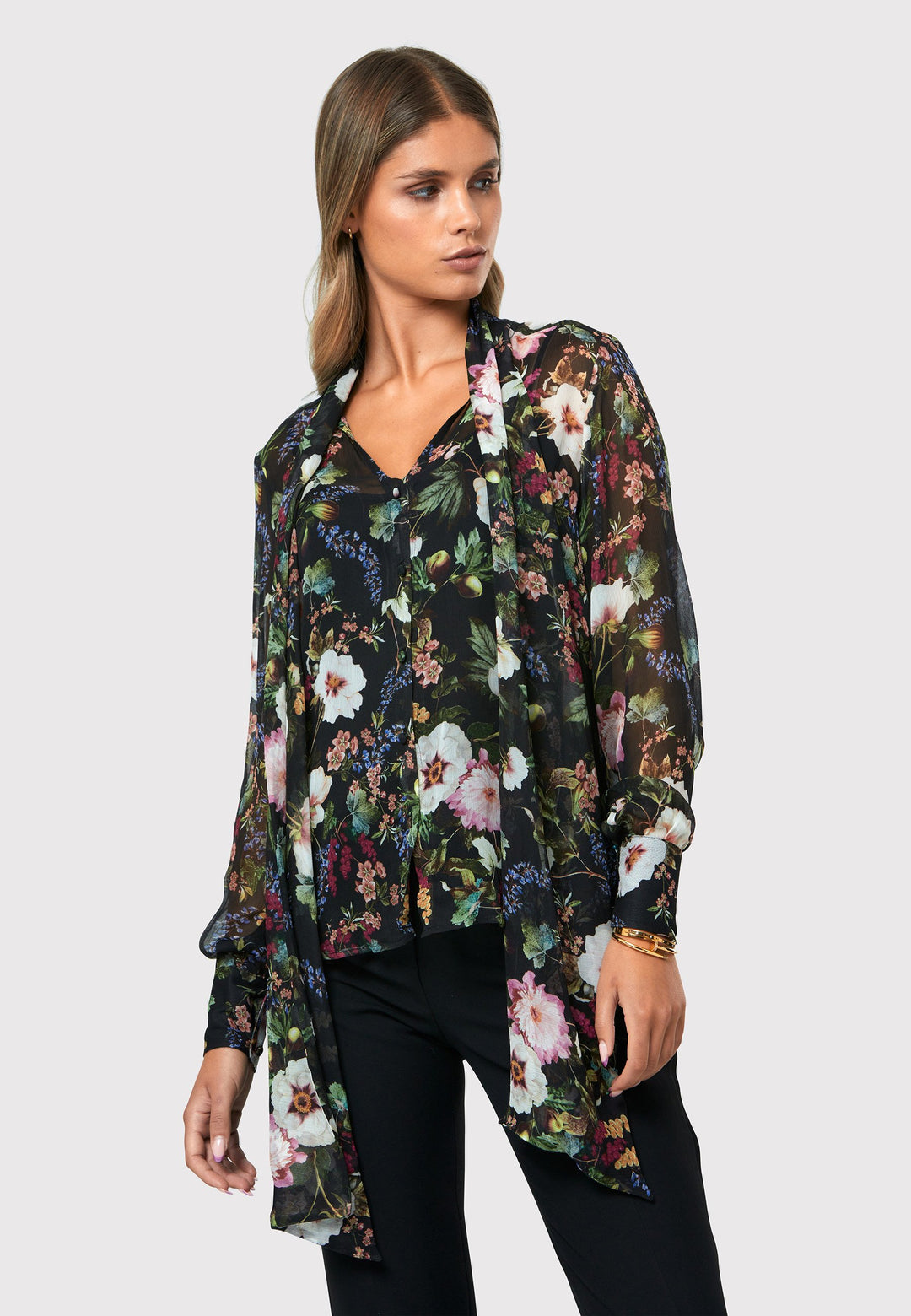 Introducing the Lorelei Floral Noir Print Blouse, a captivating blend of elegance and versatility. This blouse showcases a beautiful black-based floral print, adding a touch of sophistication to any outfit. The pussy bow neck tie, atop a flattering v-neckline, offers a versatile styling option. Wear it tied for a polished and feminine look or leave it down for a more relaxed feel. The button-down front adds a classic element, while the full-length sleeves and thick button-down cuffs exude refinement. 