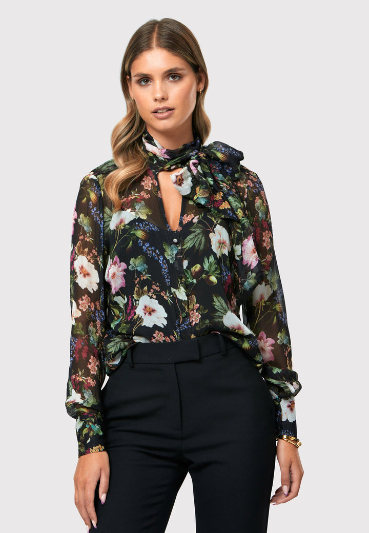 Introducing the Lorelei Floral Noir Print Blouse, a captivating blend of elegance and versatility. This blouse showcases a beautiful black-based floral print, adding a touch of sophistication to any outfit. The pussy bow neck tie, atop a flattering v-neckline, offers a versatile styling option. Wear it tied for a polished and feminine look or leave it down for a more relaxed feel. The button-down front adds a classic element, while the full-length sleeves and thick button-down cuffs exude refinement. 