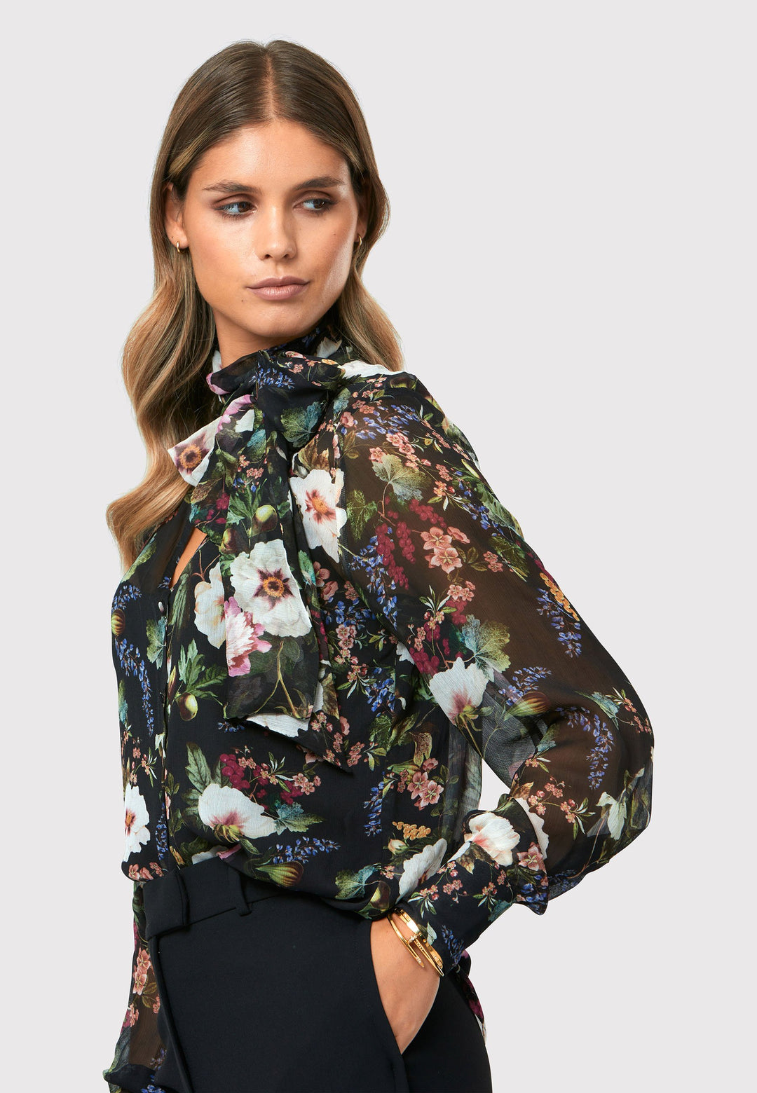 Introducing the Lorelei Floral Noir Print Blouse, a captivating blend of elegance and versatility. This blouse showcases a beautiful black-based floral print, adding a touch of sophistication to any outfit. The pussy bow neck tie, atop a flattering v-neckline, offers a versatile styling option. Wear it tied for a polished and feminine look or leave it down for a more relaxed feel. The button-down front adds a classic element, while the full-length sleeves and thick button-down cuffs exude refinement. 
