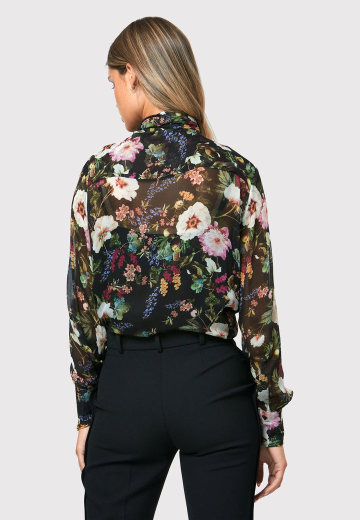 Introducing the Lorelei Floral Noir Print Blouse, a captivating blend of elegance and versatility. This blouse showcases a beautiful black-based floral print, adding a touch of sophistication to any outfit. The pussy bow neck tie, atop a flattering v-neckline, offers a versatile styling option. Wear it tied for a polished and feminine look or leave it down for a more relaxed feel. The button-down front adds a classic element, while the full-length sleeves and thick button-down cuffs exude refinement. 