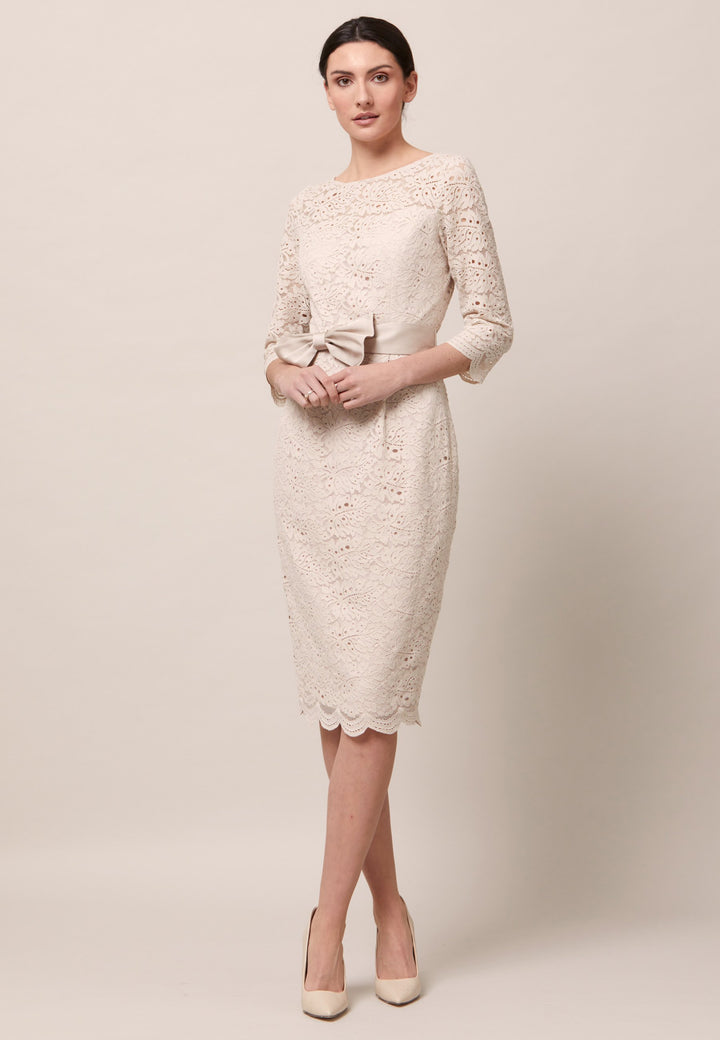Turn Heads at your upcoming occasions in the Michelle dress. Crafted in an elegant lace dress in a warm oyster tone. This style fits close to the profile with a flattering finish. Engineered with pleats at the waistline to allow the fabric to fall softly over the hips. The satin bow-belt is detachable for added versatility. Features a scalloped hem and sleeves. Attending a summer wedding? Mother of the bride? Heading to the races? This is the dress for you. 