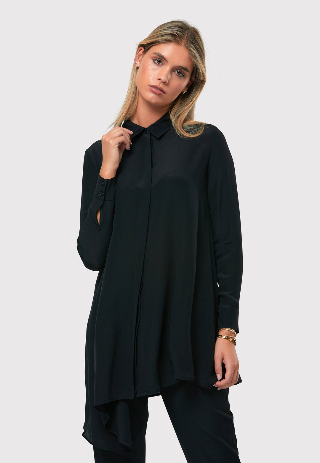 Introducing the Piper Black Silk Shirt, a timeless and versatile piece that exudes effortless sophistication. Crafted from lightweight black silk, this shirt features an asymmetrical hem for a modern twist. The full-length sleeves with cuffs add a touch of refinement. The button-down concealed placket enhances the sleek and polished look. Dress up a simple monochrome ensemble by pairing it with the Georgiana Narrow Leg Trousers in black. Embrace the elegance and versatility of the Piper Black Silk Shirt.