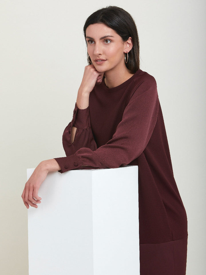 Sarah, a simple easy-fit shift dress. Crafted in a satin back crepe in rich burgundy. Features a satin raglan sleeve & a deep satin band at the hem which adds elegance to this versatile piece. Offers handy side seam pockets for added comfort and functionality. A fresh take on occasion wear.