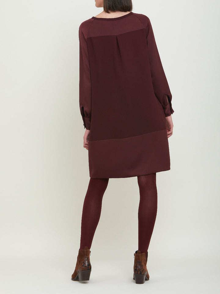 Sarah, a simple easy-fit shift dress. Crafted in a satin back crepe in rich burgundy. Features a satin raglan sleeve & a deep satin band at the hem which adds elegance to this versatile piece. Offers handy side seam pockets for added comfort and functionality. A fresh take on occasion wear.