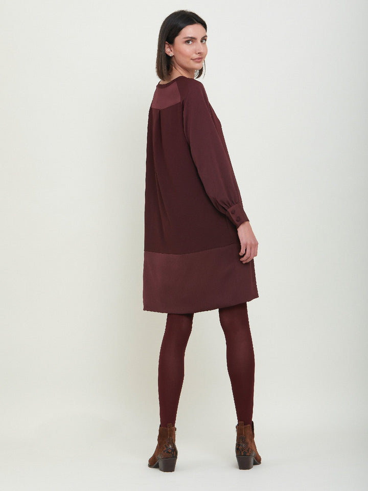 Sarah, a simple easy-fit shift dress. Crafted in a satin back crepe in rich burgundy. Features a satin raglan sleeve & a deep satin band at the hem which adds elegance to this versatile piece. Offers handy side seam pockets for added comfort and functionality. A fresh take on occasion wear.