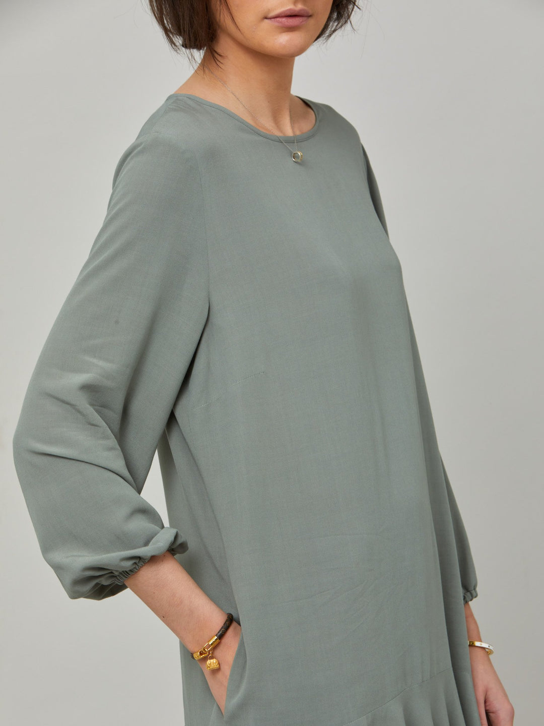 detail of Sheila, a great everyday dress. Crafted in our fluid lichen green viscose crepe. A flirty knee-grazing shift dress with a soft elasticated cuff sleeve that falls to a deep frill hem with a jewel neckline and key-hole back detail. For everyday comfort style with trainers. Elevate your mood with this fun piece.