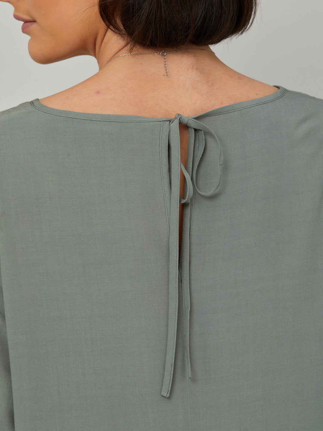 back keyhole detail of Sheila, a great everyday dress. Crafted in our fluid lichen green viscose crepe. A flirty knee-grazing shift dress with a soft elasticated cuff sleeve that falls to a deep frill hem with a jewel neckline and key-hole back detail. For everyday comfort style with trainers. Elevate your mood with this fun piece.