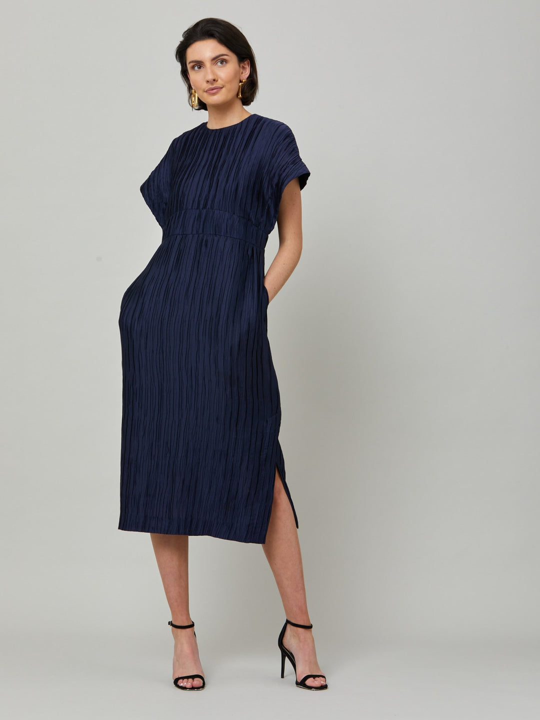 The Elegant Shiv dress redefined in a navy polished pleated fabric. An easy-fitting silhouette that falls to the mid-calf and features a side slit, pockets, and an elegant key-hole back neck detail. . Attending a summer wedding? Mother of the bride? Heading to the races? This is the dress for you.