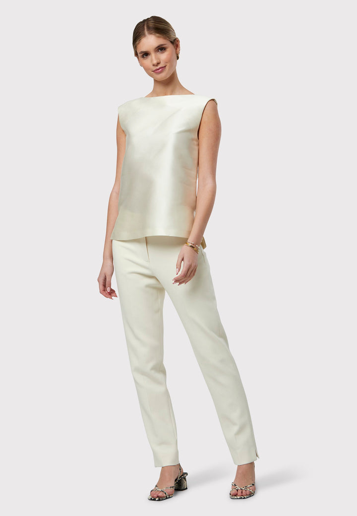 Stella Ivory Top, a sleeveless foundation piece to complement our ivory suiting or stand out as a chic standalone piece. Adorned in an ivory hue with a delicate sheen, it showcases two side slits and a central back zip. A seamless choice for embracing spring with undeniable sophistication.