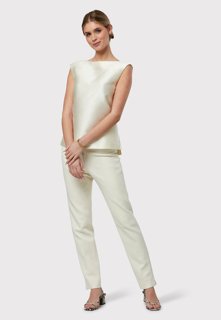 Stella Ivory Top, a sleeveless foundation piece to complement our ivory suiting or stand out as a chic standalone piece. Adorned in an ivory hue with a delicate sheen, it showcases two side slits and a central back zip. A seamless choice for embracing spring with undeniable sophistication.