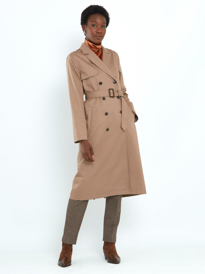 Camel trench coat double-breasted, classic collar and revere, gun flap, back vent, jetted pockets, and buckle belt. Fabricated in shower-resistant cotton poplin