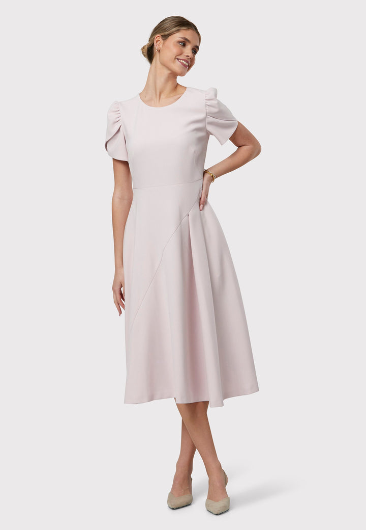 The Vera Soft Pink Dress is a captivating fit-and-flare piece. This feminine round-neck dress showcases a flared skirt that falls to a flattering mid-calf length, complete with practical pockets. The sleeves are adorned with intricate overlapping details, adding a unique touch of interest.
