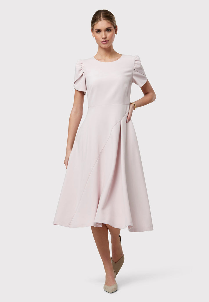 The Vera Soft Pink Dress is a captivating fit-and-flare piece. This feminine round-neck dress showcases a flared skirt that falls to a flattering mid-calf length, complete with practical pockets. The sleeves are adorned with intricate overlapping details, adding a unique touch of interest.