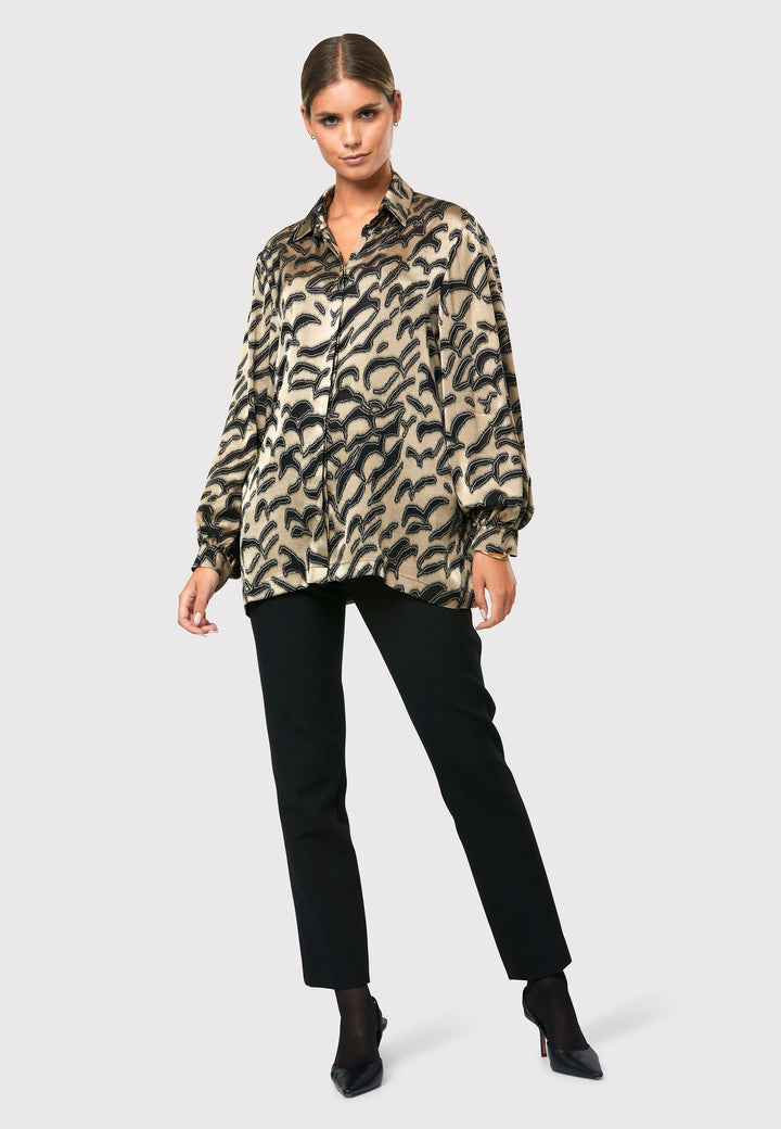 Introducing the Viola Devore Shirt, a stunning and luxurious piece that will make a statement in your wardrobe. This shirt features a captivating gold satin fabric adorned with black abstract details, creating a visually striking design. The voluminous sleeves elegantly flow into a tight buttoned cuff, adding a touch of sophistication. With its slightly dropped shoulders, this shirt offers a relaxed yet stylish fit. 